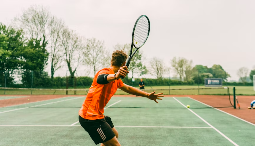 man in orange t shirt and black shorts playing lawn tennis
